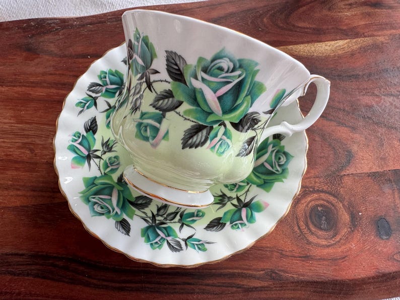 May include: A white teacup and saucer with a green and white floral pattern. The cup and saucer have a gold trim.