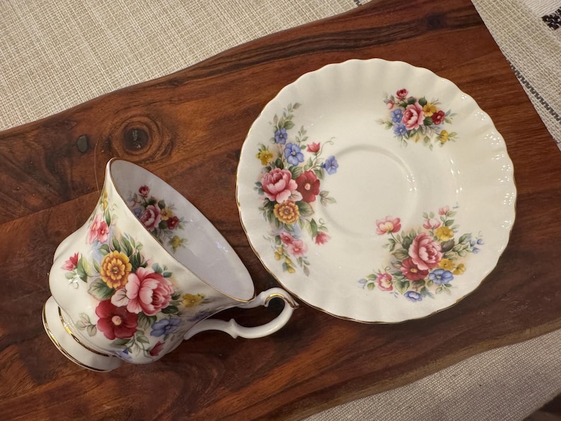 May include: A white teacup and saucer with a floral pattern. The cup and saucer have a delicate, scalloped edge. The floral pattern features pink, red, yellow, and blue flowers.