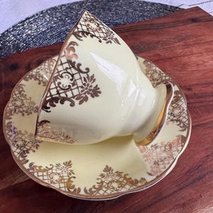 May include: A vintage teacup and saucer set with a delicate floral design in gold on a pale yellow background.