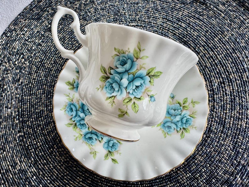 May include: A white teacup and saucer with a blue floral pattern. The cup has a delicate handle and a scalloped rim. The saucer has a gold trim.
