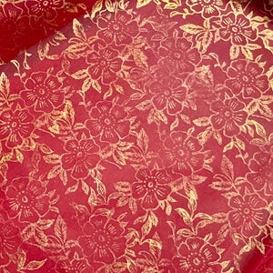 May include: Red wrapping paper with a gold floral pattern. The flowers are stylized and have a delicate design.