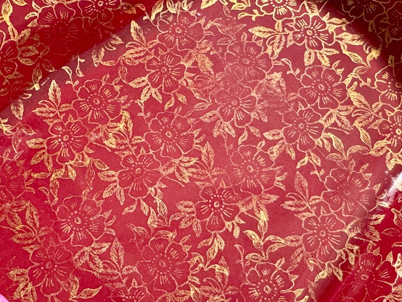 May include: Red wrapping paper with a gold floral pattern. The flowers are stylized and have a delicate design.
