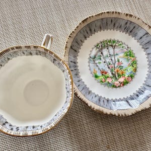 Pu&ograve; includere: Una tazzina da t&egrave; e un piattino bianchi con un design a forma di betulla. Il piattino ha un motivo a corteccia di betulla grigio e bianco con un bordo dorato. La tazzina da t&egrave; ha un motivo abbinato attorno al bordo. Il centro del piattino presenta una scena colorata di una foresta di betulle con un lago sullo sfondo.
