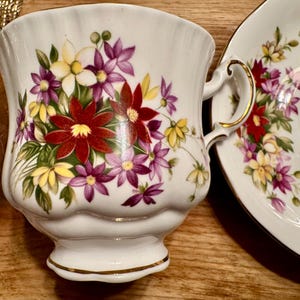 May include: A white teacup and saucer with a floral pattern. The pattern features red, yellow, and purple flowers on a white background.