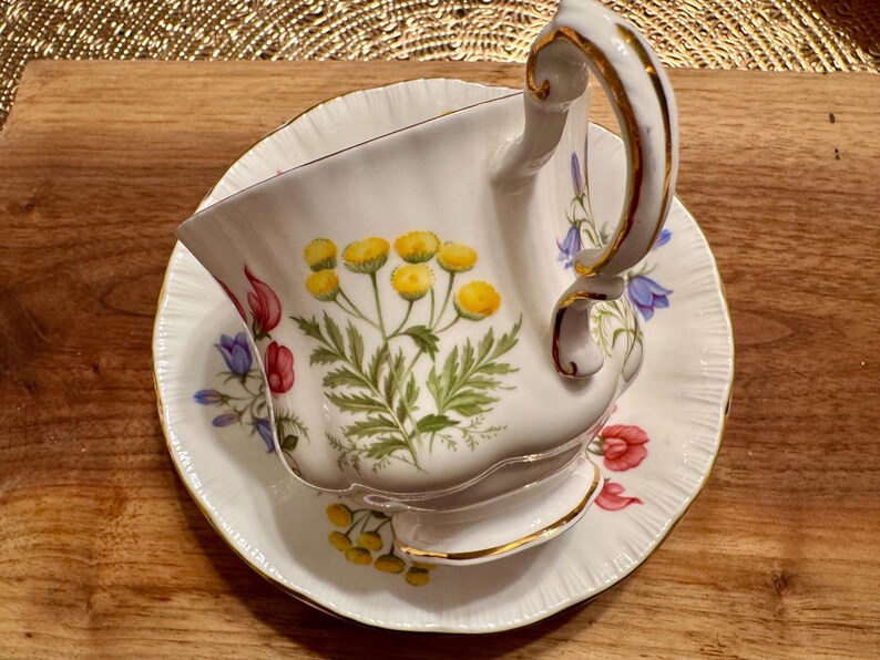 May include: A white teacup and saucer with a floral pattern. The cup has a gold rim and a delicate handle. The saucer has a scalloped edge and a floral pattern.