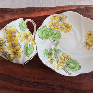 May include: A white teacup and saucer set with a floral design. The design features yellow flowers and green leaves on a white background.