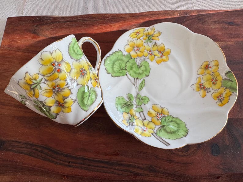 May include: A white teacup and saucer set with a floral design. The design features yellow flowers and green leaves on a white background.