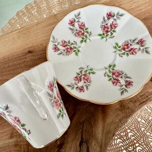 May include: A white teacup and saucer set with a floral pattern. The cup and saucer are decorated with pink and green flowers.