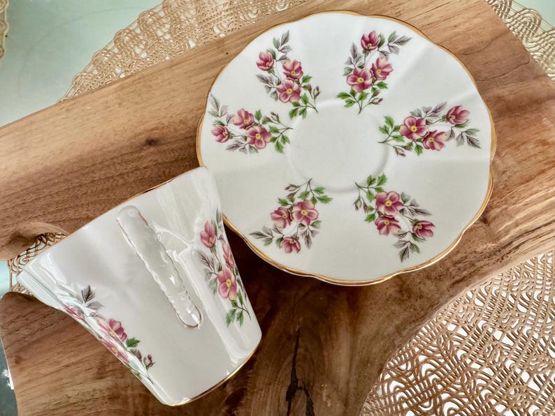 May include: A white teacup and saucer set with a floral pattern. The cup and saucer are decorated with pink and green flowers.