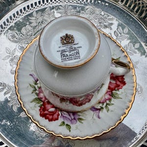 May include: A vintage teacup and saucer set with a floral pattern in red and purple, accented with gold trim. The teacup is upside down on the saucer, resting on a silver tray.