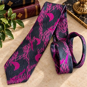Puede incluir: Una corbata con una base de color gris carb&oacute;n oscuro y un patr&oacute;n repetitivo de lunas crecientes de color magenta vibrante y formas estilizadas similares a hojas. La tela tiene un brillo sutil y el dise&ntilde;o se distribuye por toda la pieza.