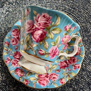 K&ouml;nnte beinhalten: Ein blaues und wei&szlig;es Tee-Set mit einem Blumenmuster aus rosa Rosen. Die Teetasse hat einen goldenen Rand.