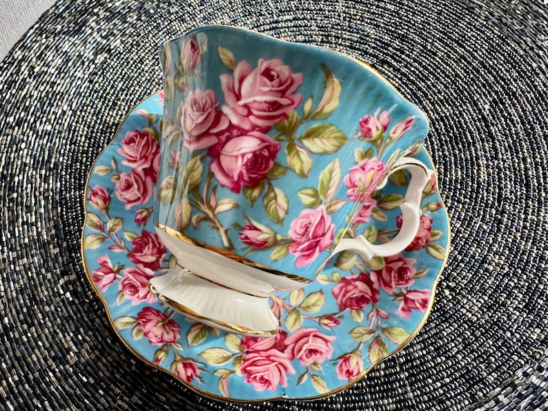 K&ouml;nnte beinhalten: Ein blaues und wei&szlig;es Tee-Set mit einem Blumenmuster aus rosa Rosen. Die Teetasse hat einen goldenen Rand.