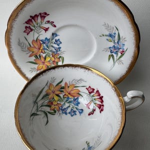 May include: A white teacup and saucer with a gold rim and a floral pattern of yellow, orange, blue, and red flowers.