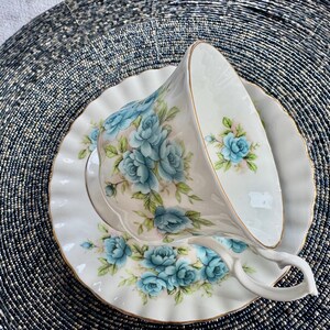 May include: A white teacup and saucer with a blue floral pattern. The cup and saucer have a gold trim around the edge.