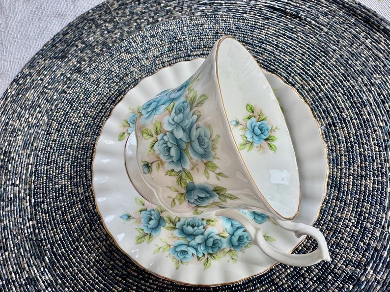 May include: A white teacup and saucer with a blue floral pattern. The cup and saucer have a gold trim around the edge.