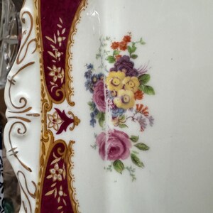 May include: A white porcelain serving platter with a burgundy and gold border. The center of the platter features a floral design with pink, yellow, and purple flowers.
