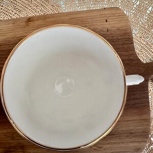 May include: A white teacup with a gold rim. The teacup is sitting on a wooden surface.
