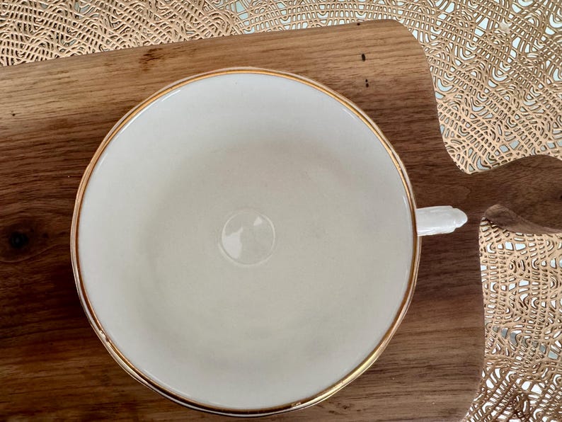 May include: A white teacup with a gold rim. The teacup is sitting on a wooden surface.