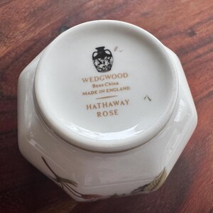 Pode incluir: Um prato de porcelana branca com formato hexagonal. A base do prato apresenta o texto "WEDGWOOD Bone China MADE IN ENGLAND HATHAWAY ROSE" e um emblema decorativo. Detalhes florais s&atilde;o vis&iacute;veis.