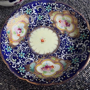 以下が含まれることがあります： 青と白の磁器製のソーサーで、花柄のデザインが施されています。ソーサーは縁が高く、波打った縁取りがされています。花柄はピンク、ブルー、グリーンの色合いで描かれており、金色のアクセントが施されています。
