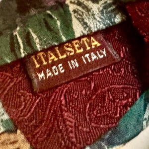 Pode incluir: Uma gravata com um padr&atilde;o paisley multicolorido em tons de verde, bord&ocirc; e dourado. Na parte de tr&aacute;s, uma etiqueta de tecido castanho est&aacute; cosida, exibindo o texto ITALSETA e MADE IN ITALY em letras brancas sobre o tecido.