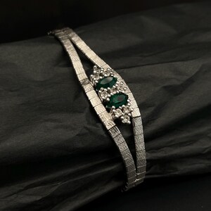 May include: A silver bracelet with a double row of links and a cluster of emerald green stones set in silver.