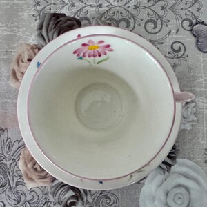 May include: A white teacup and saucer set with a pink floral design. The cup has a pink rim and handle, and the saucer features a matching floral pattern. The set is designed for tea or coffee.