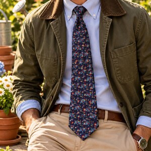 May include: A navy blue necktie featuring a repeating pattern of small red, white, and blue elephants, worn with a light blue button-down shirt, an olive green jacket with a brown corduroy collar, and khaki trousers with a brown leather belt.