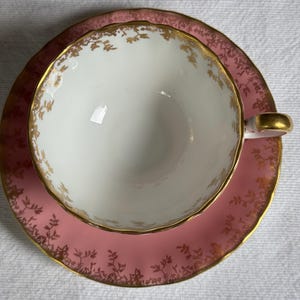 Peut inclure: Un service &agrave; th&eacute; vintage compos&eacute; d'une tasse et d'une soucoupe. La tasse est blanche avec des bordures dor&eacute;es et une anse dor&eacute;e. La soucoupe est rose avec des motifs floraux dor&eacute;s. Id&eacute;al pour les go&ucirc;ters.