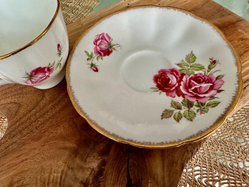 Pu&ograve; includere: Un set da t&egrave; bianco con bordo dorato e un motivo floreale di rose rosa.