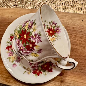 May include: A white teacup and saucer with a floral pattern in shades of red, pink, and yellow. The cup and saucer have a gold trim.
