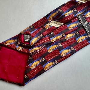 May include: An Ermenegildo Zegna necktie featuring a repeating pattern of golf bags on a background of alternating dark red textured stripes and blue stripes. The tie has a solid dark red lining and includes a black brand label and care tag.