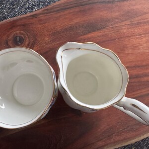 Pu&ograve; includere: Un set di due tazze da t&egrave; in porcellana bianca con bordi dorati e motivi floreali blu. Le tazze sono su una superficie di legno.