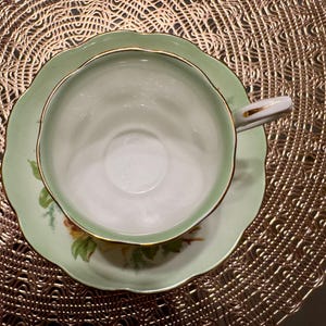 May include: A green and white teacup and saucer set with a gold trim. The saucer has a floral design.
