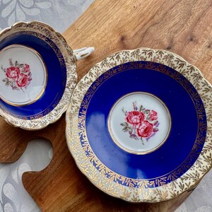 May include: A blue and gold teacup and saucer set with a floral design. The cup and saucer are decorated with a gold trim and a floral pattern in shades of pink and white.