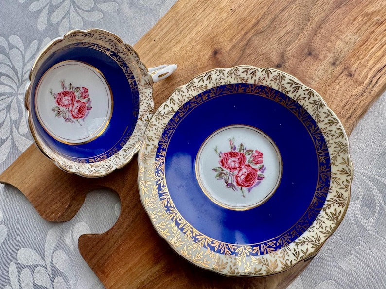 May include: A blue and gold teacup and saucer set with a floral design. The cup and saucer are decorated with a gold trim and a floral pattern in shades of pink and white.