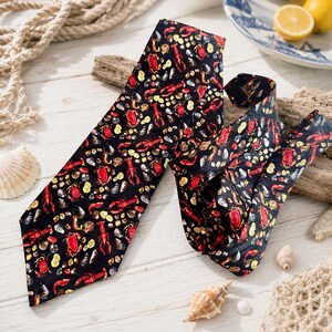 Puede incluir: Una corbata negra con un patr&oacute;n repetitivo de langostas rojas, cangrejos y varias conchas marinas en tonos blanco, gris y amarillo. La tela tiene un acabado suave y muestra un estampado detallado de vida marina en toda la superficie.