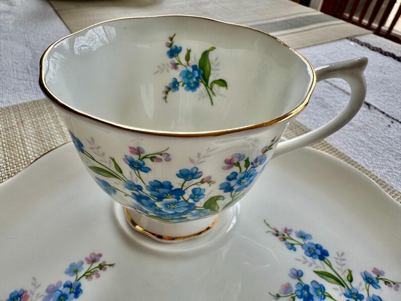 May include: A white teacup and saucer set with a blue and white floral pattern. The cup has a gold rim and the saucer has a floral design around the edge.
