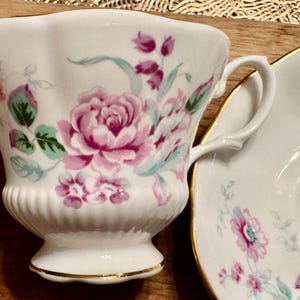 May include: A white teacup and saucer with a floral pattern. The cup has a scalloped rim and a delicate handle. The saucer has a matching floral design.
