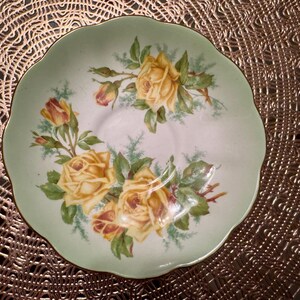 May include: A green and white teacup saucer with a floral design featuring yellow roses and green leaves.