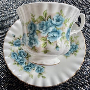 May include: A white teacup and saucer with a blue floral pattern. The teacup has a fluted edge and a handle. The saucer has a scalloped edge.