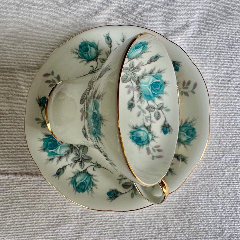 Peut inclure: Un service &agrave; th&eacute; vintage compos&eacute; d'une tasse et d'une soucoupe. La tasse et la soucoupe en porcelaine blanche sont orn&eacute;es de motifs floraux de roses turquoise et de bordures dor&eacute;es. Un ensemble de th&eacute; classique.
