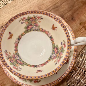 May include: A white teacup and saucer with a floral pattern and gold trim. The cup has a handle and the saucer has a scalloped edge.