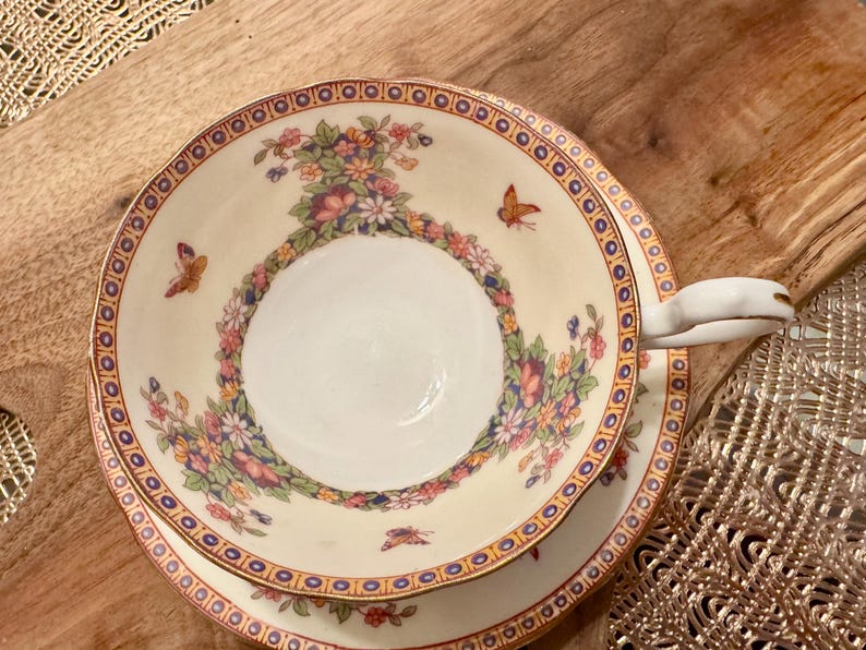May include: A white teacup and saucer with a floral pattern and gold trim. The cup has a handle and the saucer has a scalloped edge.