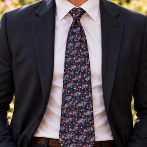 May include: A dark blue necktie featuring a repeating pattern of small, colorful elephants wearing red hats and carrying umbrellas, worn with a crisp white dress shirt and a dark navy blue suit jacket.