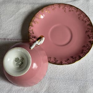 Peut inclure: Service &agrave; th&eacute; rose avec des d&eacute;tails dor&eacute;s. La tasse et la soucoupe sont roses avec des motifs floraux dor&eacute;s sur les bords. L'int&eacute;rieur de la tasse est blanc avec un logo. Un ensemble de style classique.