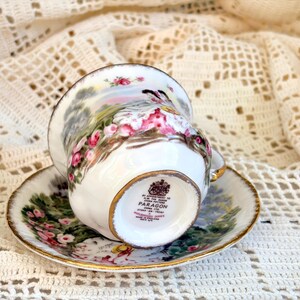 May include: A white porcelain teacup and saucer set featuring a floral pattern with pink roses and green foliage. The base of the cup displays the text: BY APPOINTMENT TO H.M. THE QUEEN CHINA POTTERS PARAGON CHINA LTD STOKE-ON-TRENT MADE IN ENGLAND.