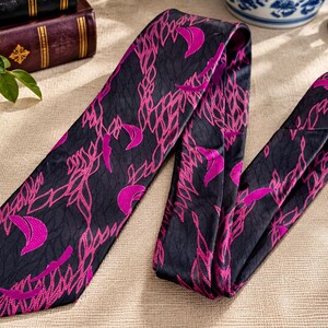 Puede incluir: Una corbata con una base de color gris carb&oacute;n oscuro y un patr&oacute;n repetitivo de formas de media luna en magenta vibrante y contornos entrelazados en forma de hoja. La tela tiene un acabado sutil y finamente texturizado en toda la pieza.