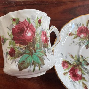 May include: A white teacup and saucer set with a floral design featuring red roses and green leaves.